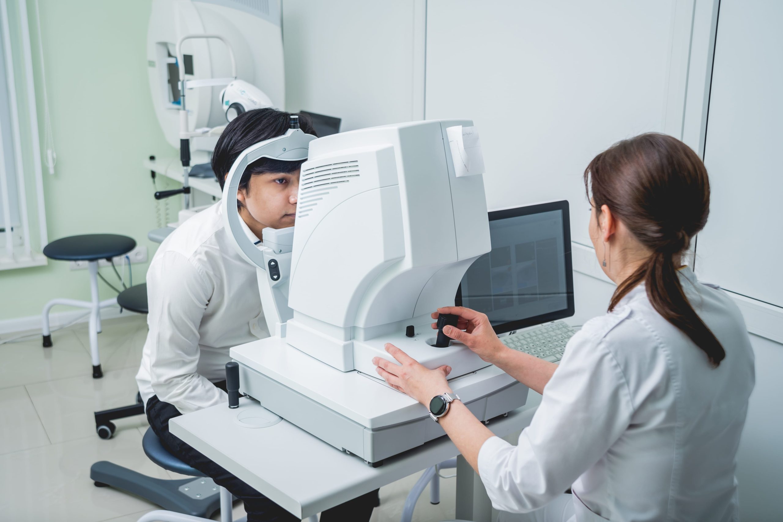 Patient undergoing a comprehensive eye exam using a vision testing machine with an optometrist in a clinic.